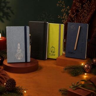 Vier individuell bedruckte Notizbücher mit Logo in Grau, Schwarz, Grün und Blau mit Gummiband und Stift als Weihnachtsgeschenkidee für Kunden und Mitarbeiter