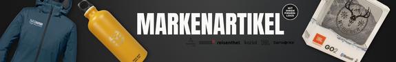 Auf schwarzem Hintergrund sind drei gebrandete Markenartikel zu sehen: eine blaue Softshelljacke mit Logo auf der Brust, eine gelbe Trinkflasche aus Metall mit weißem Aufdruck und ein kompakter Bluetooth-Lautsprecher in Originalverpackung. Daneben steht der Schriftzug „MARKENARTIKEL“ mit Logos bekannter Hersteller.