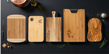 Fünf, in Form und Holzart, unterschiedliche Schneidebretter auf Schieferplatte aus Vogelperspektive fotografiert