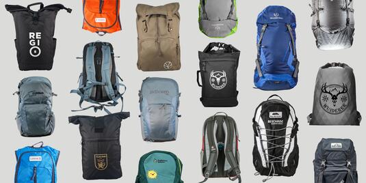 Mehrere Rucksäcke in unterschiedlichen Farben, Formen und Designs sind auf grauem Hintergrund angeordnet. Zu sehen sind Modelle aus Stoff oder Nylon mit verschiedenen Verschlüssen, Tragesystemen und aufgedruckten Logos. Die Rucksäcke variieren zwischen sportlich, funktional und alltagstauglich.