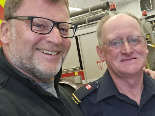 Zwei Personen der North Queens Fire Association in Fahrzeughalle im Rahmen einer T-Shirt-Spendenaktion für Kanada von Firma Lerche: