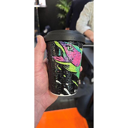 Ein Werbe-Becher aus Porzellan mit spannender Haptik im Puzzle-Design über ein buntes Motiv gelegt.