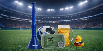 Mehrere Fußball-Werbeartikel mit Logo im Stadion: blaue Vuvuzela und Ball mit Sortimo Logo, Brotbox Moose, Quietscheente mit Deutschland-Trikot und Bierkrug.