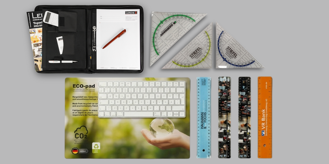 Verschiedene Büro-Werbeartikel: Schreibmappe, Geodreiecke, Lineale mit Logodruck mehrerer Firmen.