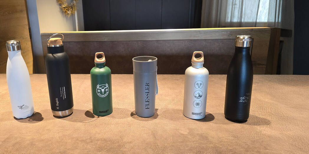 Viele unterschiedliche Trinkflaschen mit Logos stehen nebeneinander auf einem Tisch. 