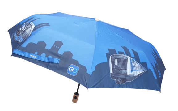 Blauer Taschenschirm mit schwarzem Gestänge und hellem Griff. Auf dem Schirm sind grafische Darstellungen von U-Bahn-Zügen und einer Stadtsilhouette in dunklen Blautönen zu sehen, dazu kleine Logos und eine Webadresse.