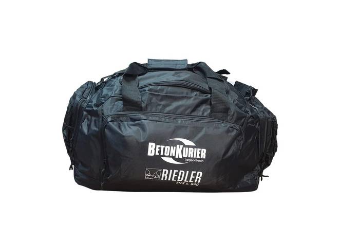 Schwarze Sport- oder Reisetasche mit mehreren Reißverschlussfächern und zwei Tragegriffen. Auf der Vorderseite ist ein weißer Logoaufdruck mit den Schriftzügen „BetonKurier“ und „Riedler“ zu sehen.