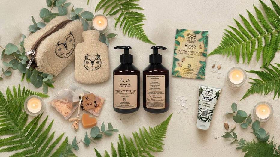 Verschiedene Wellness Werbeartikel auf hellem Hintergrund mit Eukalyptus und Fahn-Blättern und Kerzen als Szenerie.