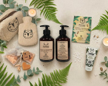 Verschiedene Wellness Werbeartikel auf hellem Hintergrund mit Eukalyptus und Fahn-Blättern und Kerzen als Szenerie.