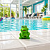 Kleiner grüner Frosch mit Logo auf dem Bauch am Poolrand sitzend und im Hintergrund türkises Wasser in heller, freundlicher Schwimmbad-Atmosphäre