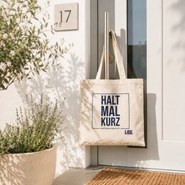 Naturfarbene UBL-Königsdorf-Baumwolltasche mit Aufdruck „Halt mal kurz – die Demokratie hoch“ an einer Haustür in hellem Ambiente
