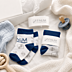 Weiß-blaue Baby-Werbesocken mit eingestricktem FINUM-Firmenlogo, Banderole und Babyaccessoires als Moodbild