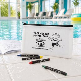 Weiße Stiftetasche mit schwarzem Transferdruck des Thermelino Kinder-Clubs und Wachsmalstiften am Beckenrand liegend.