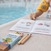 Bedrucktes Holz-Buntstifte-Set mit Logo „Therme Obernsees Kinder-Club“ neben Malbuch am Poolrand.