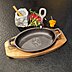 Iron Plate Gusseisenpfanne mit Logo-Brandstempel in dekorativer Food-Präsentation auf Servierplatte aus Akazienholz mit schwarzem Hintergrund