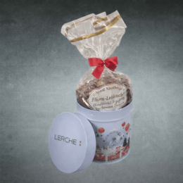 Geöffnete Dose mit weihnachtlichem Motiv, aus der in Folie verpackte Lebkuchen herausschauen, Deckel angelehnt mit Logo Lasergravur Lerche: individuell gebrandet