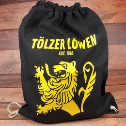 Schwarzer Textil-Werbemittel-Turnbeutel mit gelbem Logodruck der Tölzer Löwen und Kordelzugverschluss auf Holzboden