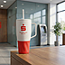 Weißer Werbethermobecher mit Henkel und roter Manschette mit Sparkasse-Bremen-Logodruck, platziert auf einem Tresen in einer Filiale.