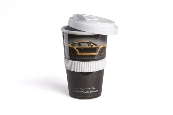 Ein schwarzer Porzellanbecher mit weißem Kunststoffdeckel und geriffelter Silikonbanderole in Weiß. Auf dem Becher ist ein goldenes Auto abgebildet, darunter steht die Aufschrift „25 Jahre Porsche Exclusive“. Der Becher steht aufrecht vor weißem Hintergrund.