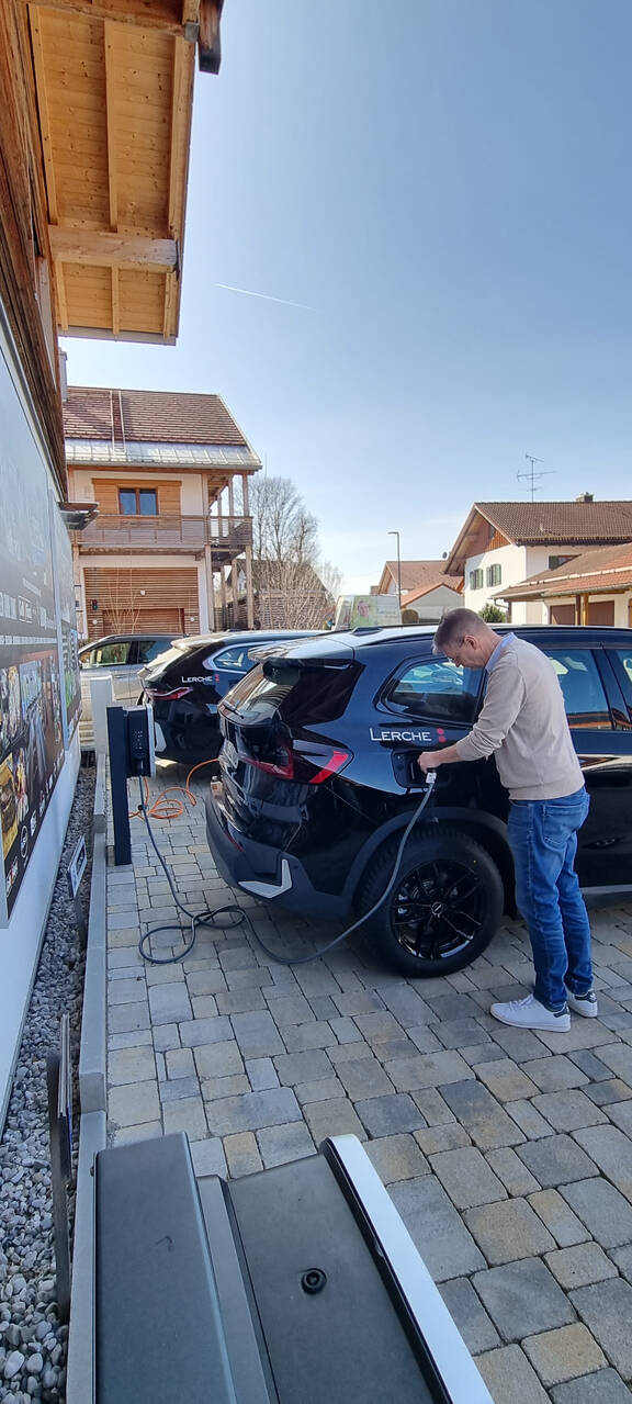 Person steht am Firmenwagen und schließt es an eine E-Ladestation an. Nachhaltigkeit im Betrieb.