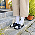 Nahaufnahme von Beinen, welche weiße Diabetikersocken mit schwarzen Sandalen darüber und gekürzter beiger Hose tragen, dargestellt auf einer Steintreppe umgeben von Grün und Pflanzen