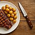 Werbe-Steakmesser mit gezahnter Edelstahlklinge und braunem Holzgriff neben einem Teller mit gegrilltem Steak und kleinen Kartoffeln auf einem Holztisch