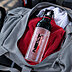 Transparente DUIX Sport Trinkflasche mit Logo und rotem Deckelring in einer grauen Sporttasche auf rotem Handtuch als sportliches Werbemittel im Alltagseinsatz